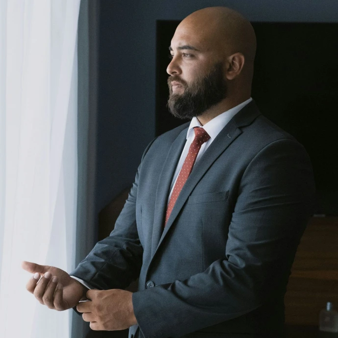 a bald man in a suit standing next to a window